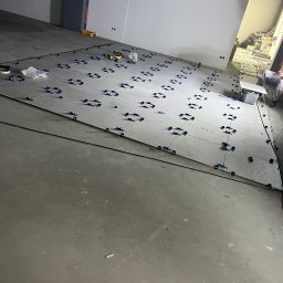 Nazarii Struk - Układanie szarych płytek z użyciem klipsów poziomujących i lasera krzyżowego. Widoczny fragment osoby układającej płytki. Praca w toku, surowy stan.