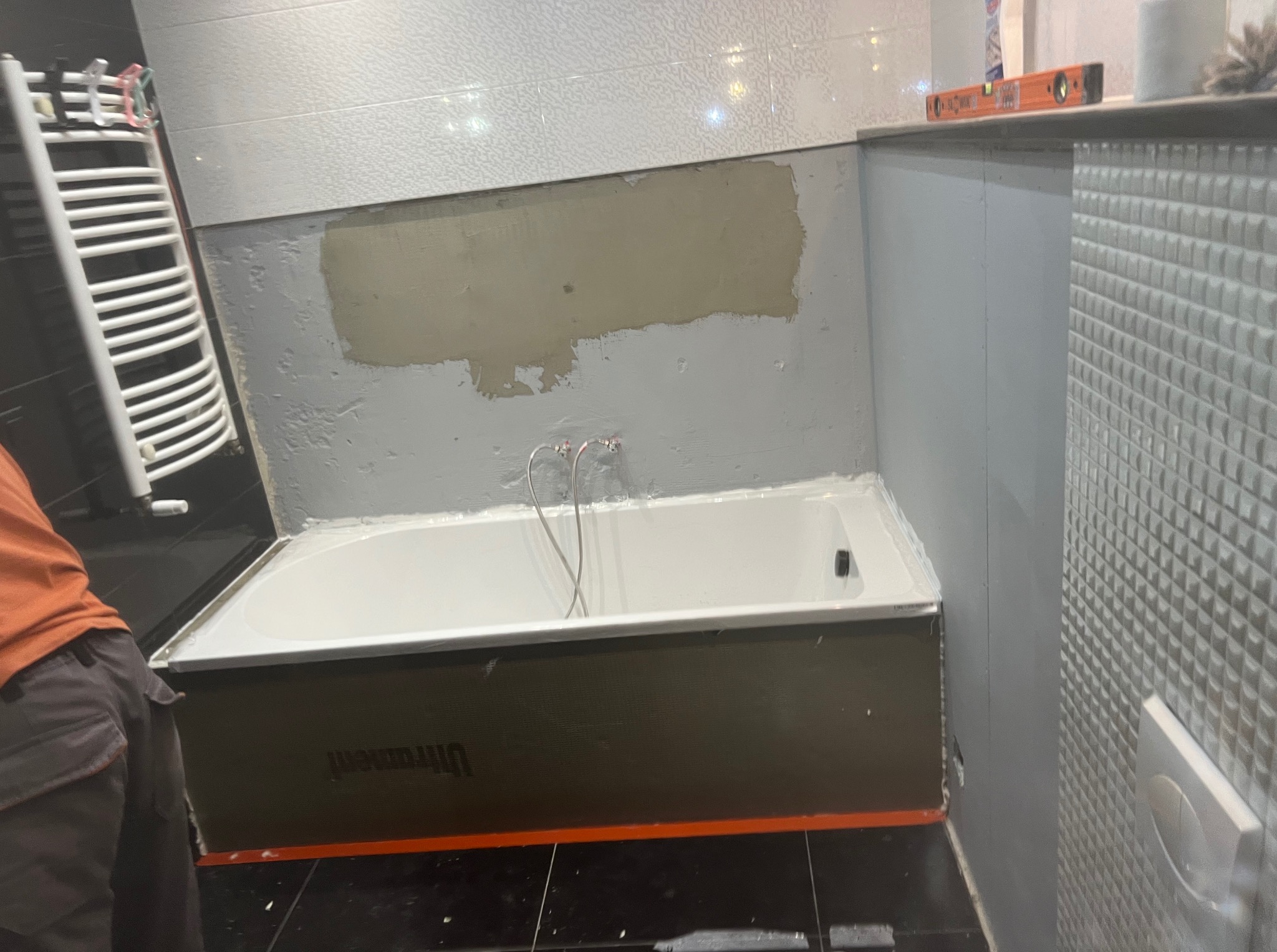 Montaż wanny w łazience z częściowo położonymi płytkami. Widoczne przygotowania do dalszych prac wykończeniowych.