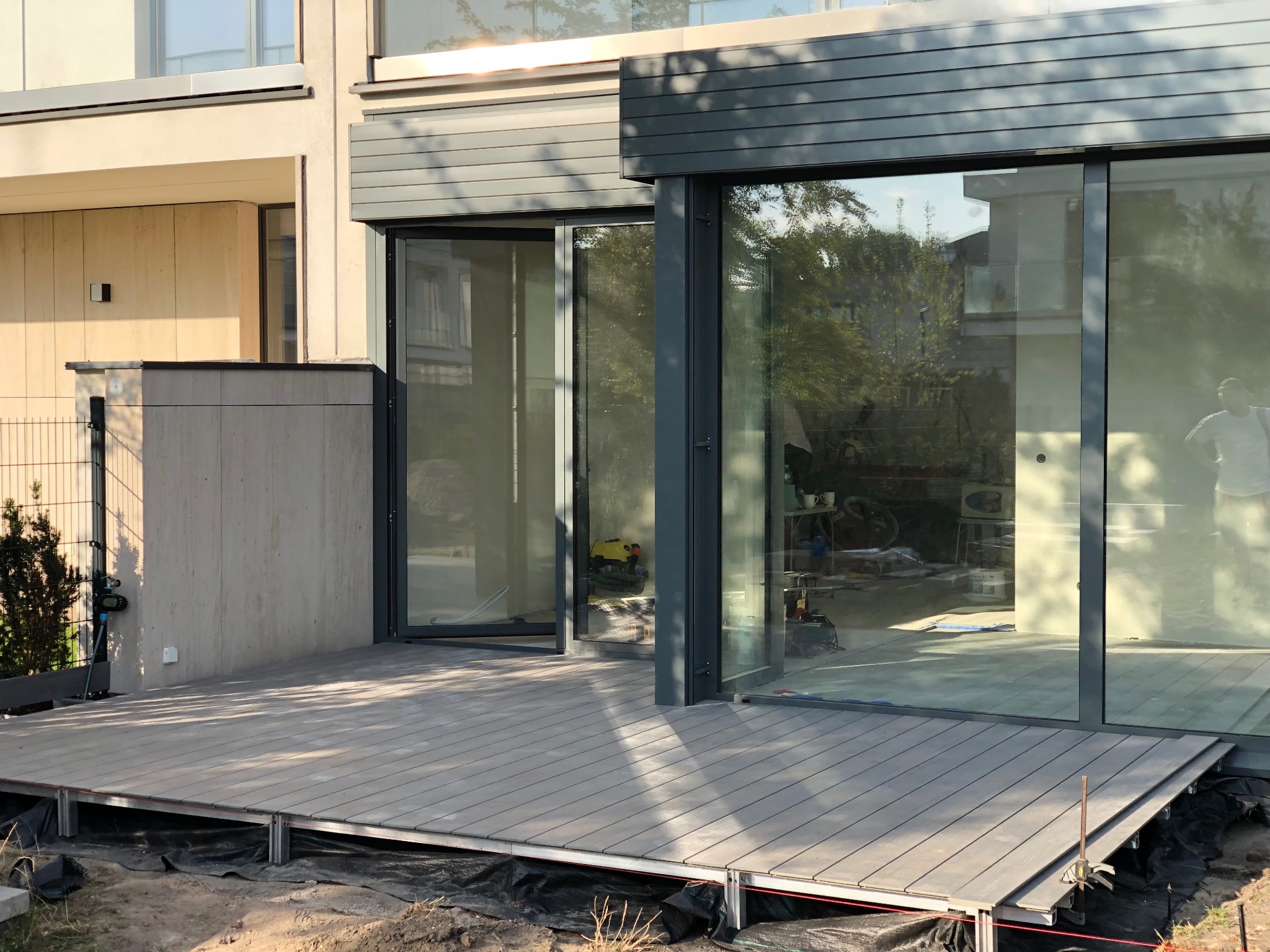 Nowoczesny taras z desek kompozytowych w Warszawie, z widoczną konstrukcją nośną i dużymi oknami przesuwnymi. Minimalistyczny design, jasne kolory.