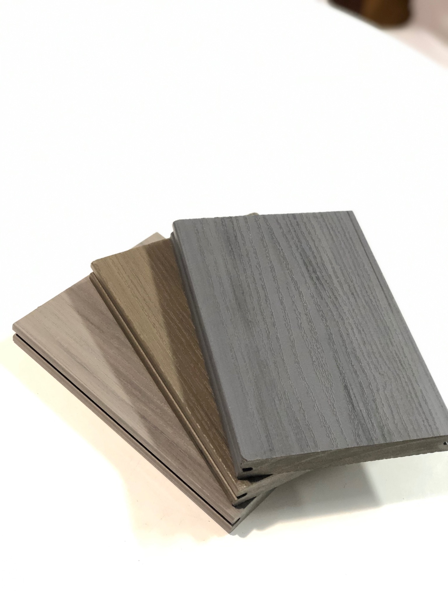 Przekrój trzech desek kompozytowych w odcieniach szarości i brązu, ukazujący strukturę drewna i system łączenia. Prezentacja materiałów na jasnym tle.