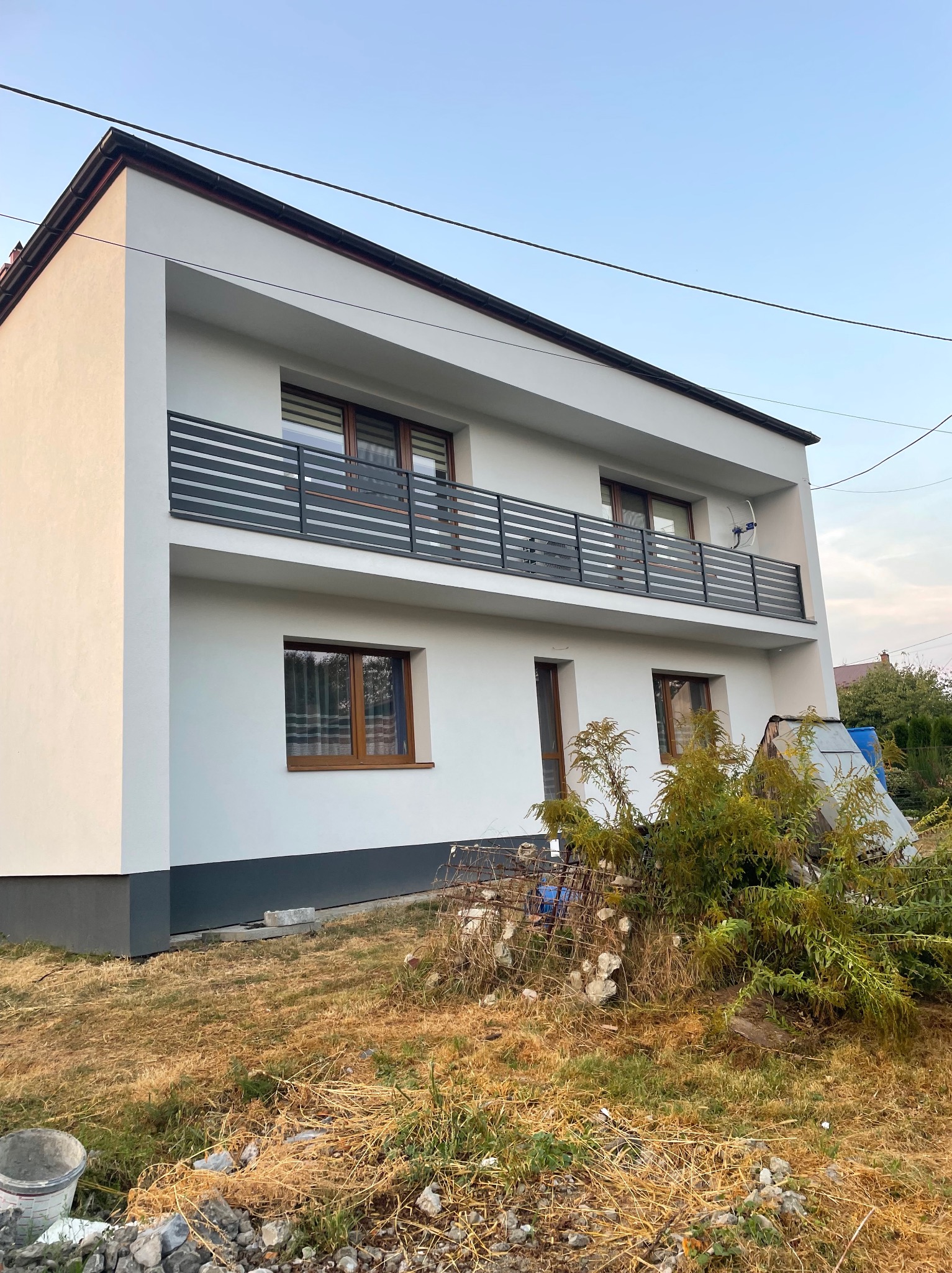 Dwupiętrowy dom z balkonami zabezpieczonymi poziomymi, metalowymi barierkami; widoczny bałagan na trawniku.