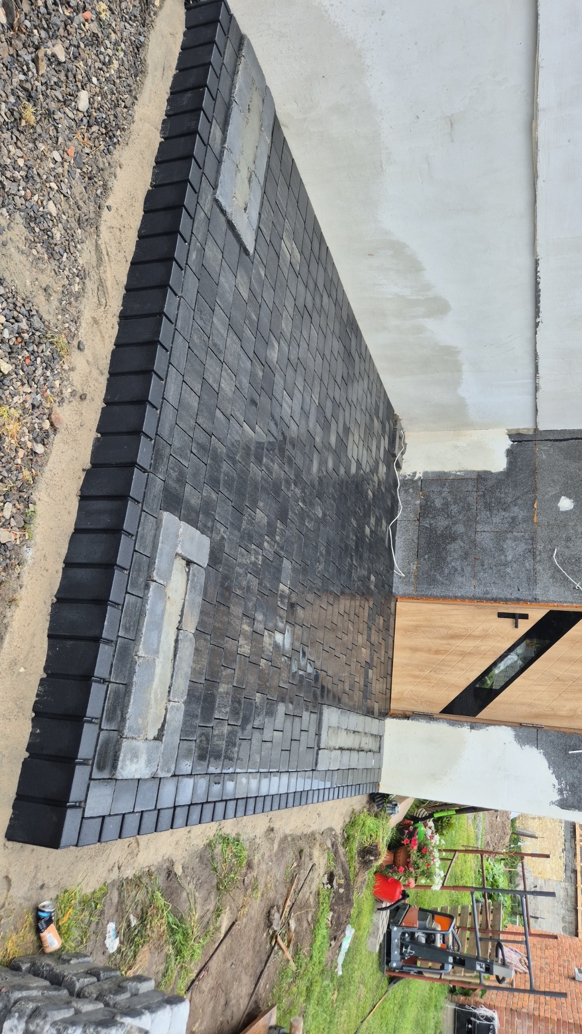 Ułożona kostka brukowa przy budynku w Pawliczce. Widoczny fragment elewacji i teren wokół, świeżo po zakończeniu prac. Kostka w odcieniach szarości.