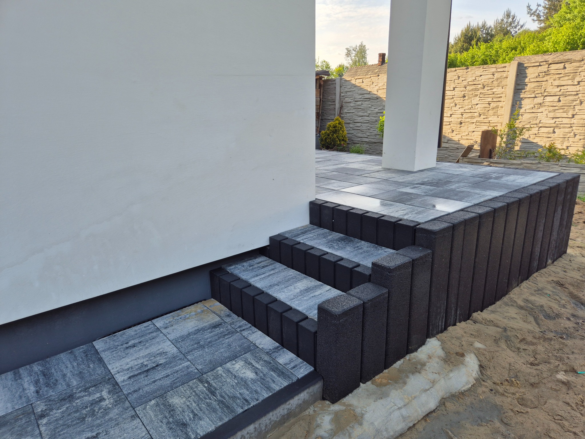 Schody z kostki brukowej prowadzące do wejścia domu, z widocznymi elementami wykończeniowymi i otoczeniem posesji.