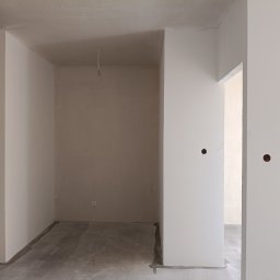 LUK-BUD Łukasz Słysz - Wnętrze w trakcie wykończenia: gładkie, białe ściany po szpachlowaniu, surowy beton na podłodze, widoczne instalacje elektryczne. Minimalizm, stonowana kolorystyka.