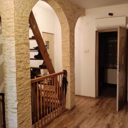LUK-BUD Łukasz Słysz - Aranżacja wnętrza z kamiennymi łukami i drewnianą podłogą. Widoczne schody z obuwiem i otwarte drzwi do pokoju. Klimatyczne oświetlenie.