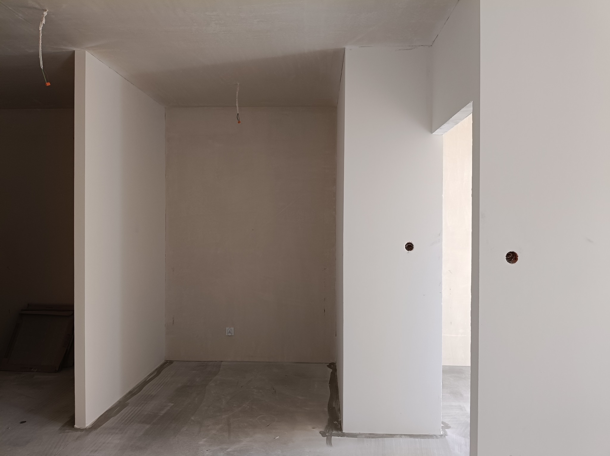 Wnętrze w trakcie wykończenia: gładkie, białe ściany po szpachlowaniu, surowy beton na podłodze, widoczne instalacje elektryczne. Minimalizm, stonowana kolorystyka.