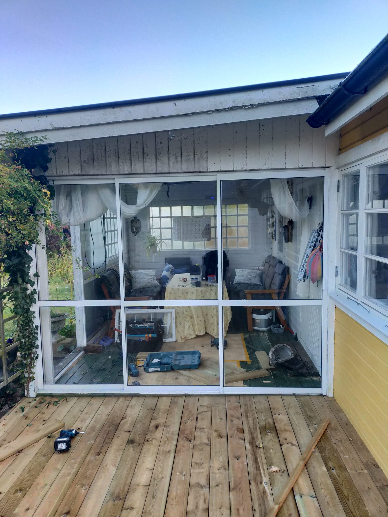 Zabudowa tarasu z widocznymi narzędziami, deskami podłogowymi i wnętrzem z meblami wypoczynkowymi.