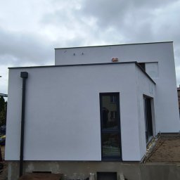 MixBud - Nowoczesny dom z białą elewacją, widoczny z zewnątrz, z czarnymi ramami okiennymi i rynną, na tle pochmurnego nieba.