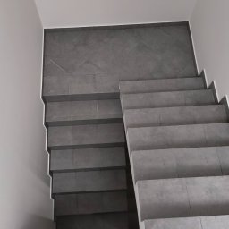 MixBud - Schody wyłożone szarymi, kwadratowymi płytkami, widok z góry, białe ściany, minimalistyczny design.