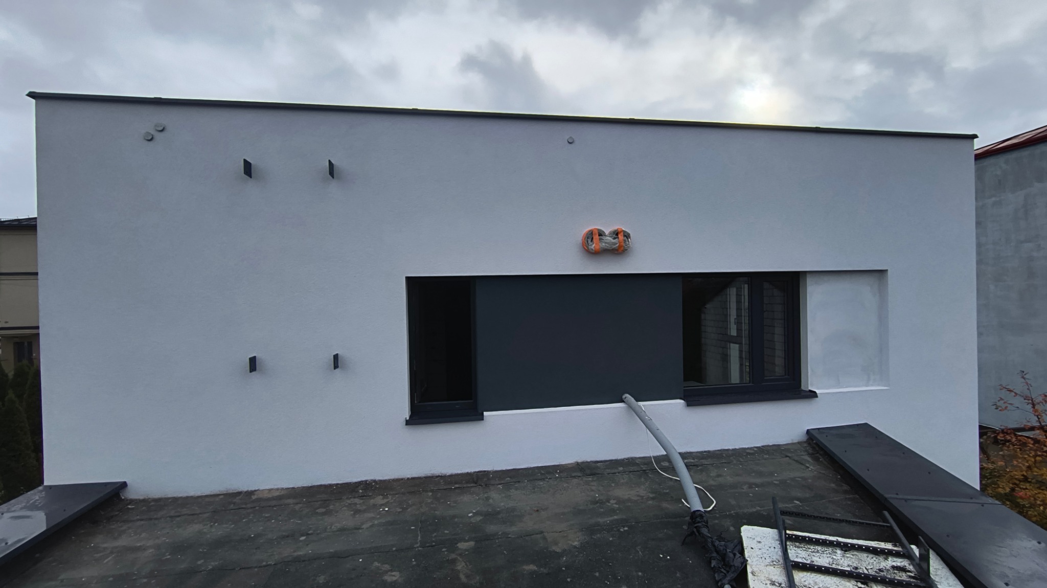 Świeżo otynkowana, szara elewacja domu jednorodzinnego z widocznymi detalami architektonicznymi i przygotowaniem do dalszych prac wykończeniowych, widok z dachu.