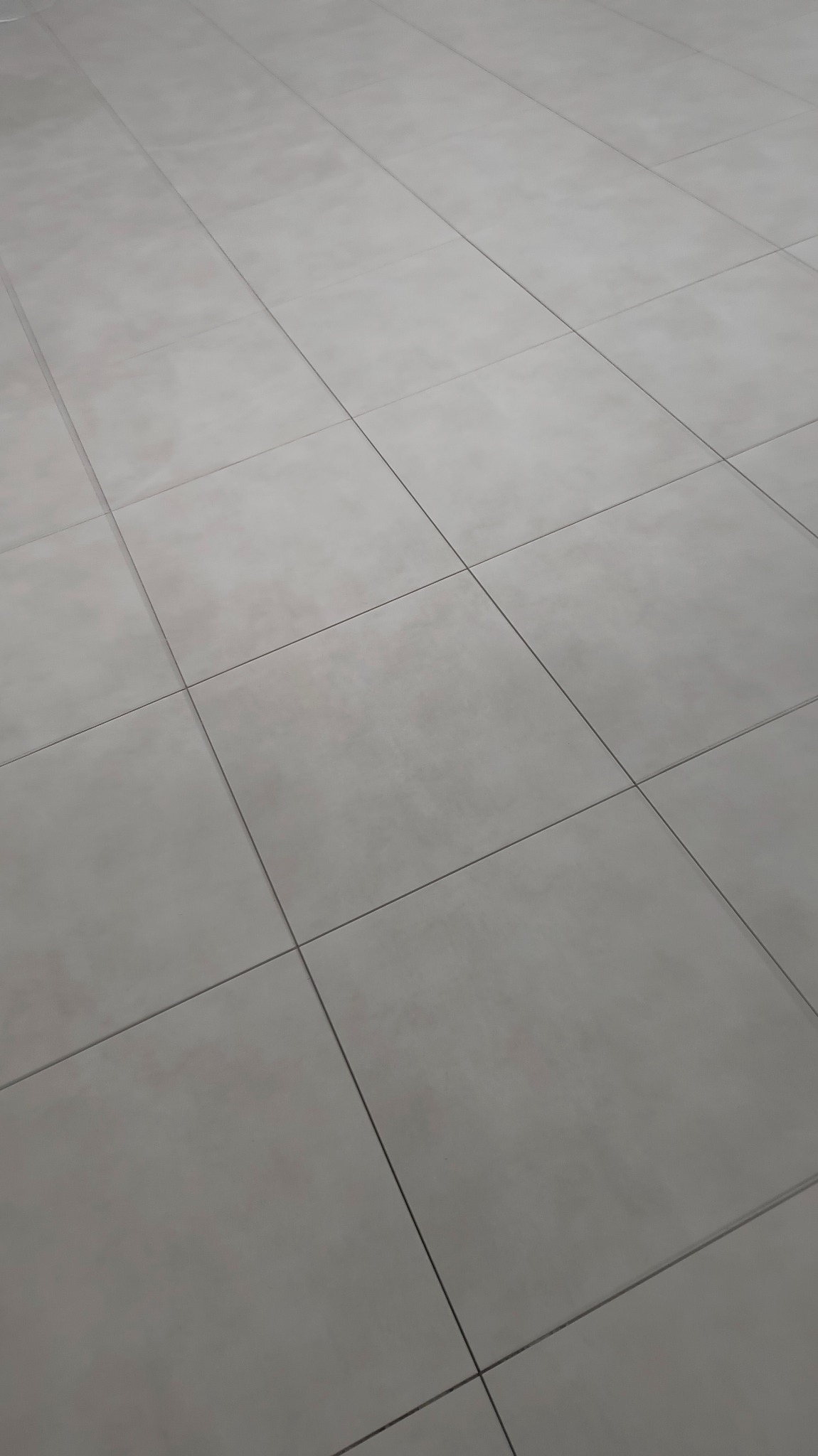 Szare, matowe płytki podłogowe ułożone w regularny wzór kwadratów, widok z góry pod kątem, minimalizm.