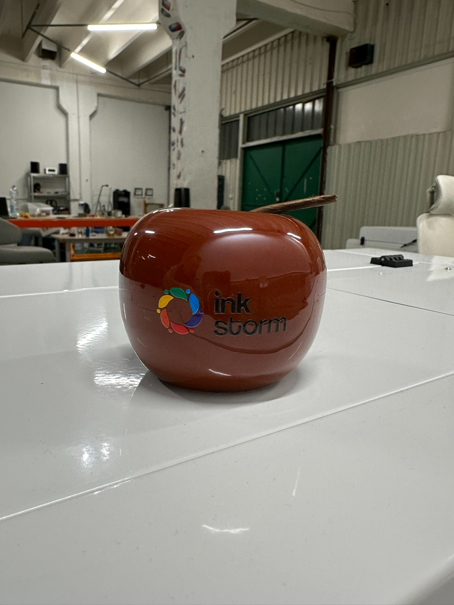 Błyszczący, brązowy, ceramiczny model jabłka z logo 'ink Storm' na białym stole w warsztacie.