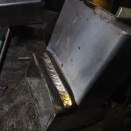 Spoina na metalowej konstrukcji z widocznymi śladami ciepła, wykonana na brudnym stole warsztatowym.