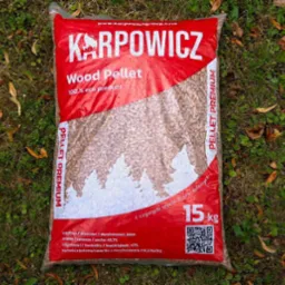 Worek 15 kg pelletu drzewnego marki Karpowicz, leżący na trawie z opadłymi liśćmi. Widoczny napis 'Wood Pellet 100% eco product' oraz parametry techniczne.