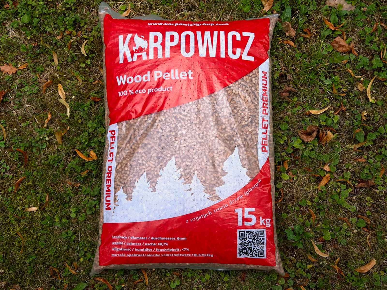 Worek 15 kg pelletu drzewnego marki Karpowicz, leżący na trawie z opadłymi liśćmi. Widoczny napis 'Wood Pellet 100% eco product' oraz parametry techniczne.