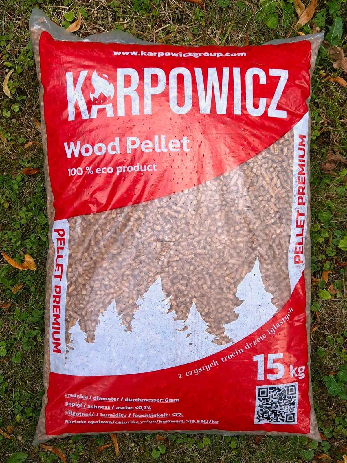 Worek 15 kg pelletu drzewnego Karpowicz Premium na trawie, z widocznym logo i informacjami o produkcie, w tym zarysem drzew iglastych.