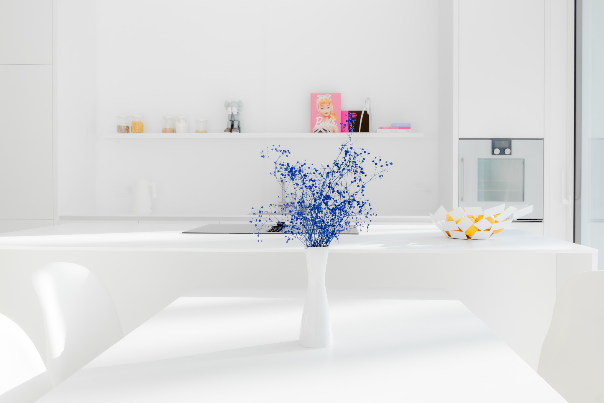 Minimalistyczna, biała kuchnia z niebieskim bukietem w wazonie na stole, owocami w ozdobnej misie i półką z dekoracjami w tle.