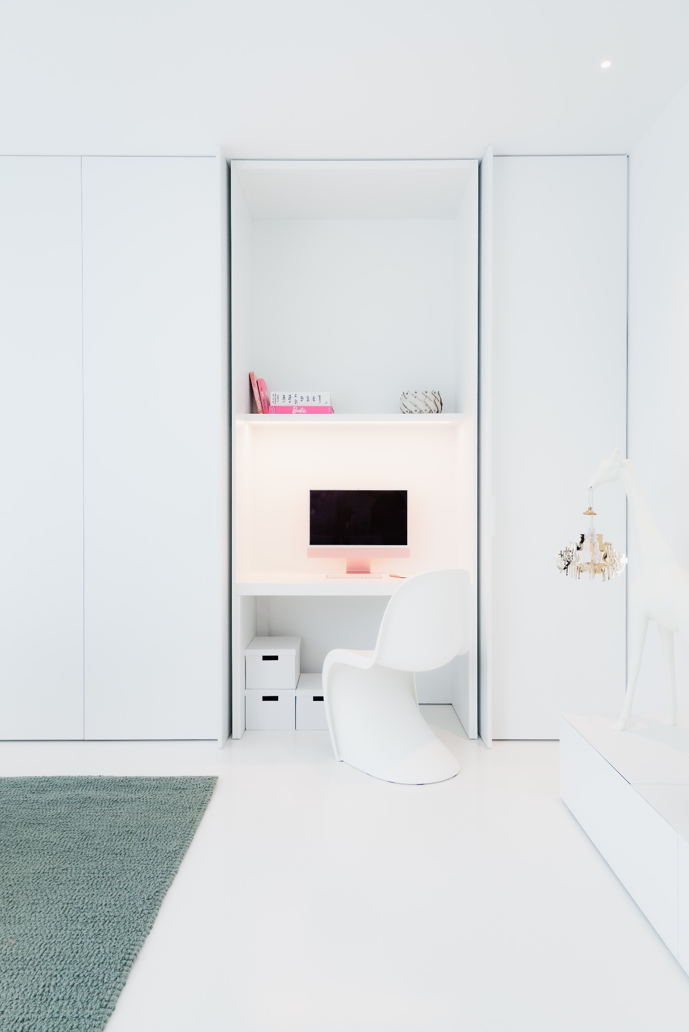 Minimalistyczne, białe wnętrze z biurkiem, krzesłem Tulip i różowym komputerem iMac, uzupełnione zielonym dywanem i figurką żyrafy z dekoracyjnym elementem