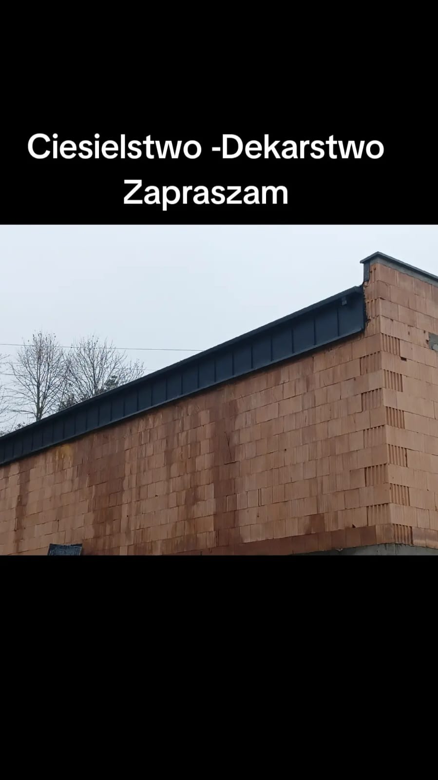 Surowy mur z cegły ceramicznej z zamontowaną obróbką blacharską na krawędzi dachu, widok z dołu na budynek w trakcie budowy.