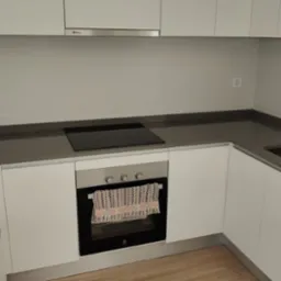 Minimalistyczna kuchnia po sprzątaniu: białe szafki, szary blat z płytą indukcyjną, drewnopodobna podłoga. Czystość i porządek w każdym detalu.