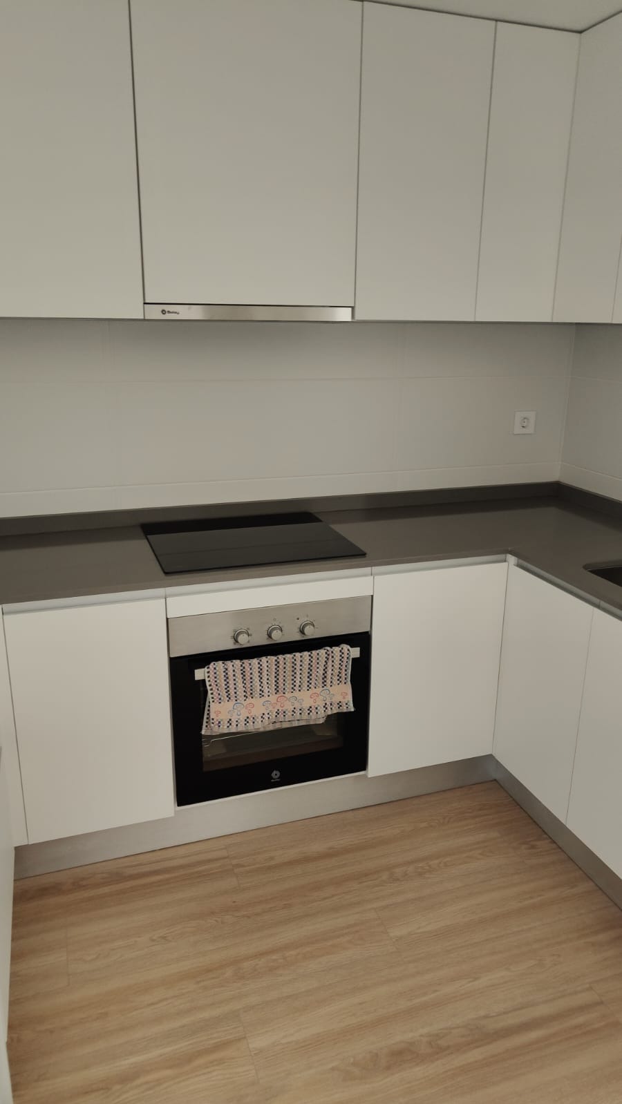 Minimalistyczna kuchnia po sprzątaniu: białe szafki, szary blat z płytą indukcyjną, drewnopodobna podłoga. Czystość i porządek w każdym detalu.