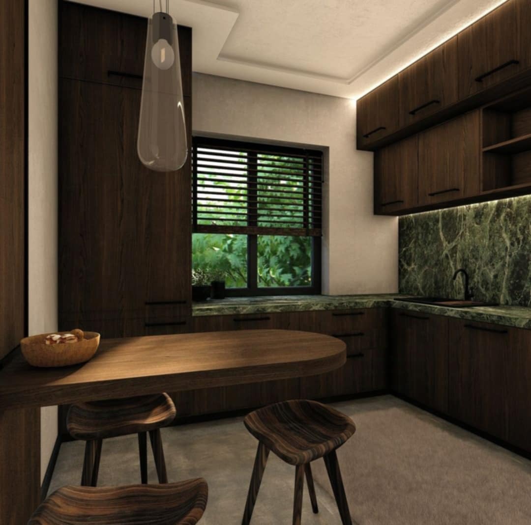 Nowoczesna kuchnia z ciemnymi drewnianymi szafkami, blatem z zielonego marmuru i drewnianymi stołkami barowymi przy zaokrąglonym blacie.