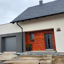 Usługi Ogólnobudowlane - Nowoczesny dom jednorodzinny z elewacją w odcieniach szarości i drewna, widoczny fragment terenu w trakcie prac wykończeniowych.