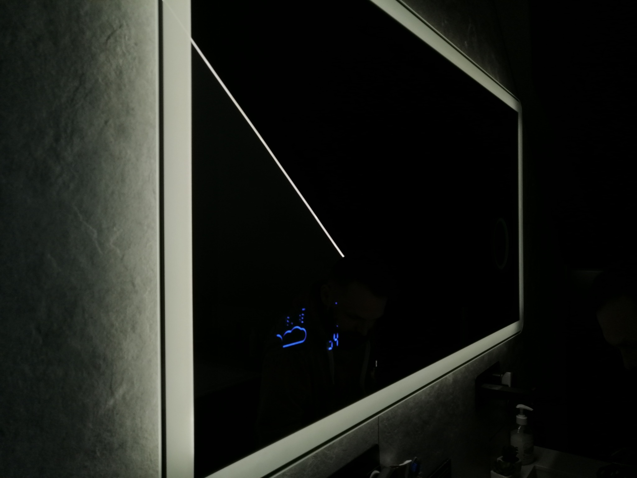 Nowoczesne oświetlenie LED w łazience z efektem lustra i wyświetlanymi ikonami pogody, na tle ściany o fakturze kamienia.