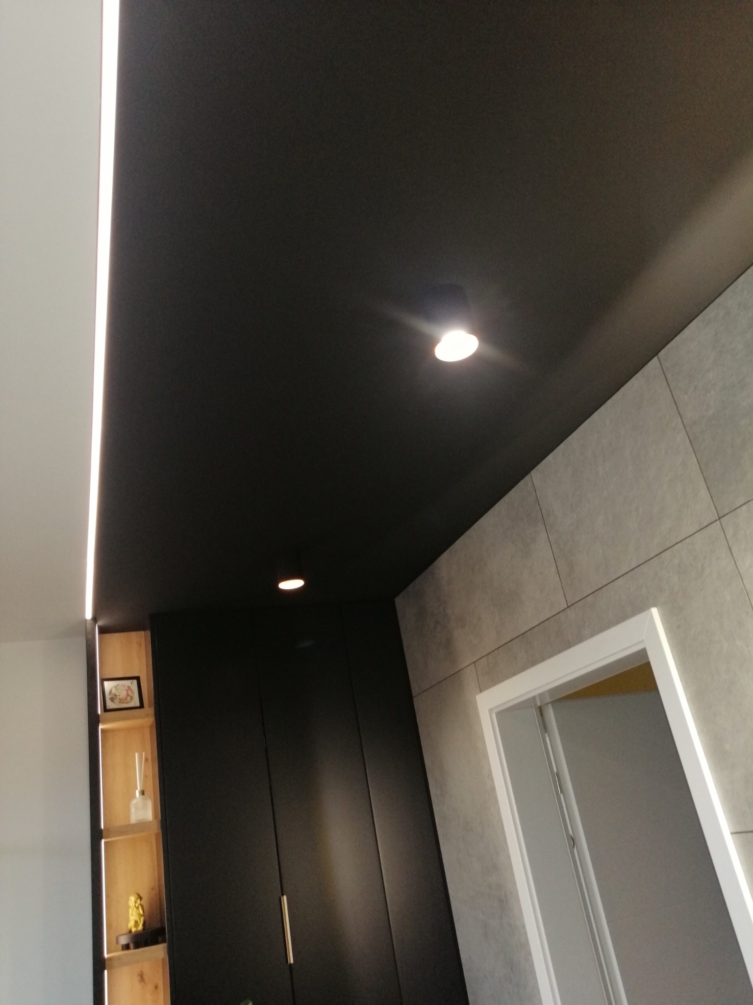 Czarne malowanie sufitu z wbudowanym oświetleniem LED, widoczne szare płytki na ścianie i zabudowa meblowa w tle.