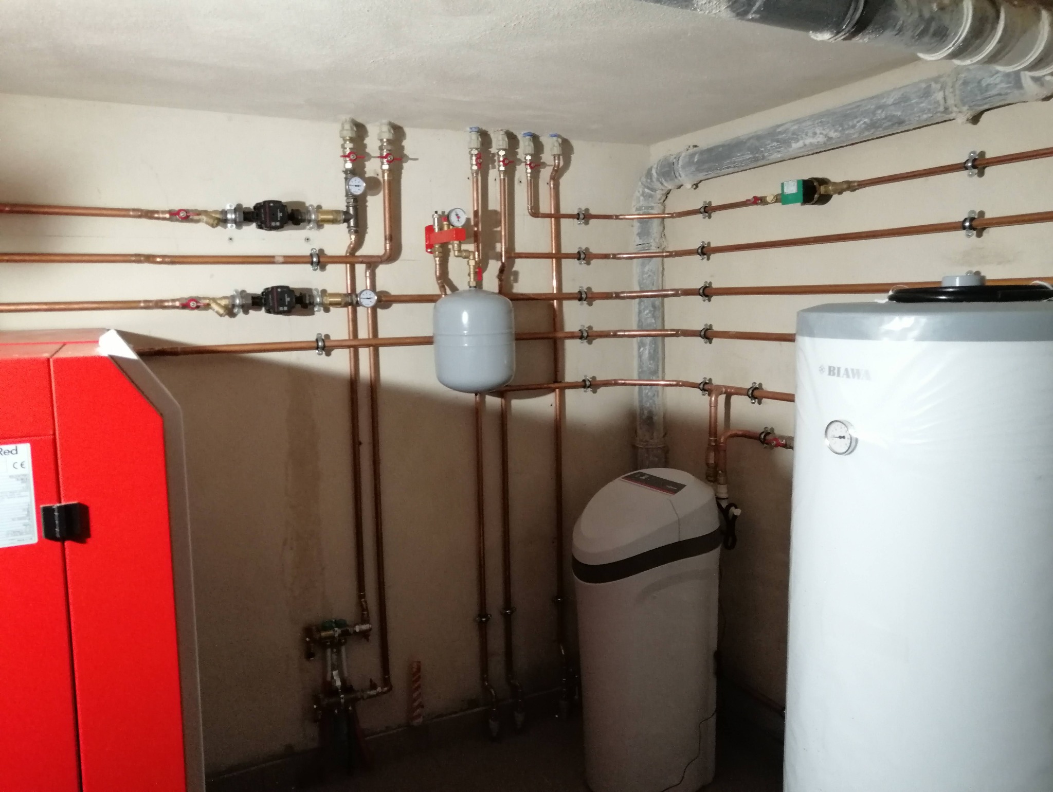 Złożona instalacja centralnego ogrzewania z miedzianymi rurami, zbiornikiem wyrównawczym, kotłem Red i zmiękczaczem wody w kotłowni.
