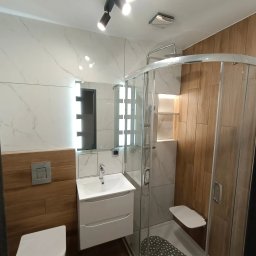 Dream House Antoni Ostrowski - Nowoczesna łazienka z kabiną prysznicową z siedziskiem, umywalką z szafką i podświetlanym lustrem, wykończona płytkami imitującymi marmur i drewno