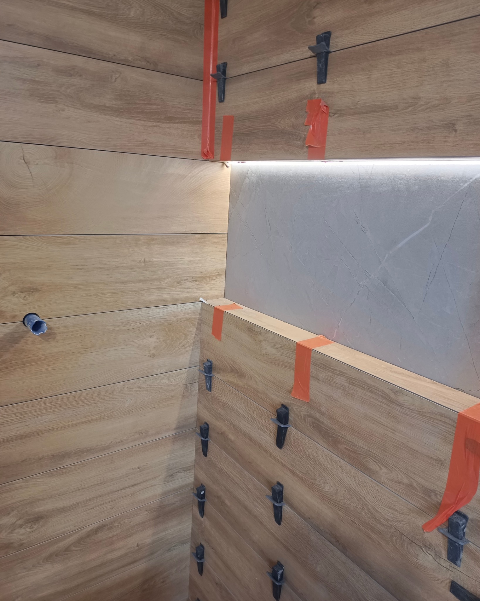 Układanie płytek imitujących drewno w łazience, widoczne klipsy poziomujące i taśma malarska zabezpieczająca narożniki.