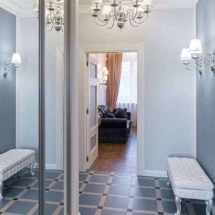 Elegancki przedpokój w odcieniach szarości z lustrzaną szafą przesuwną, kwadratową podłogą i widokiem na salon z sofą.