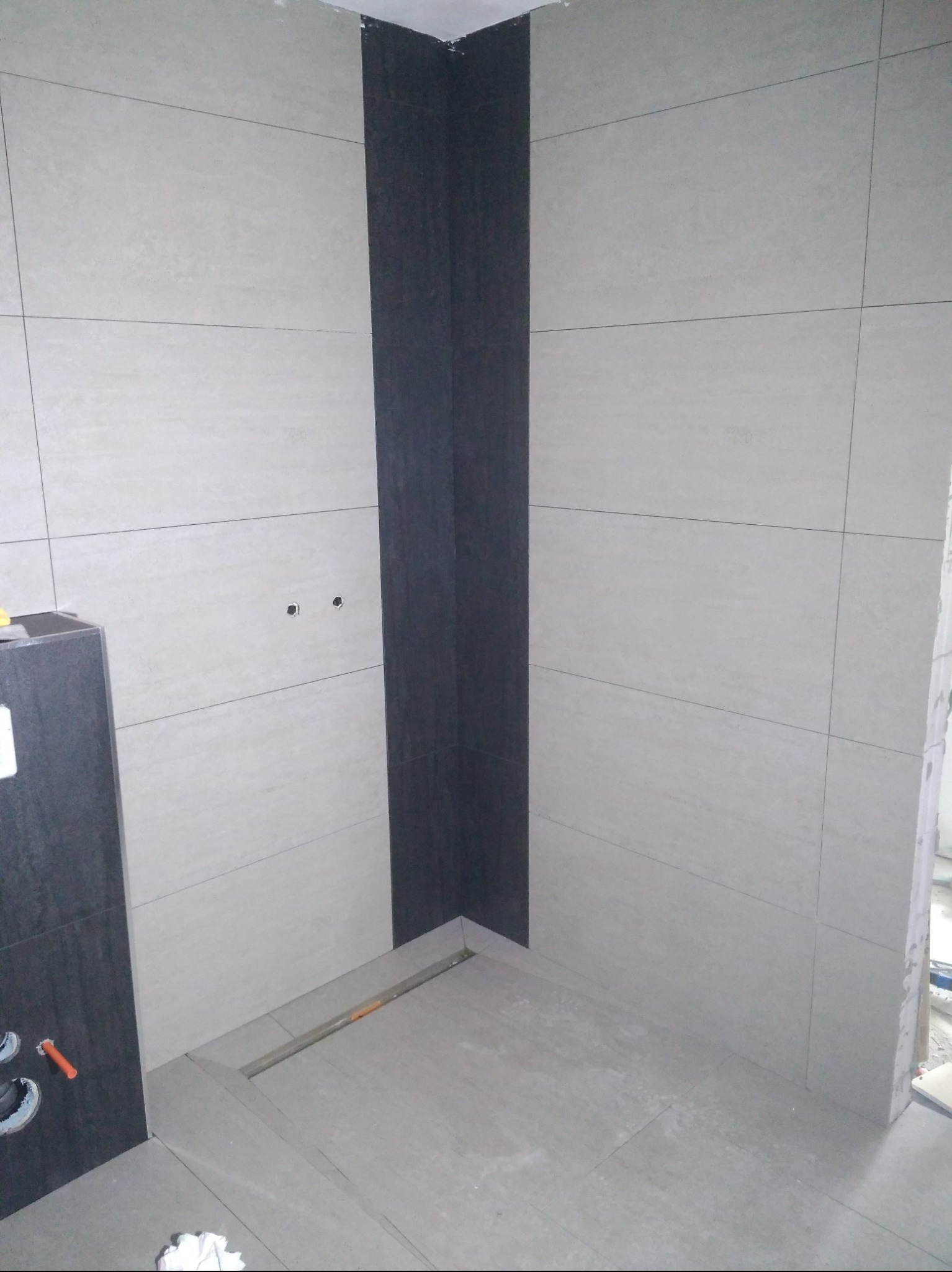 Wykończona ściana i podłoga z płytek w łazience w Pakości. Widoczny odpływ liniowy i fragment szafki pod umywalkę z ciemnymi płytkami.