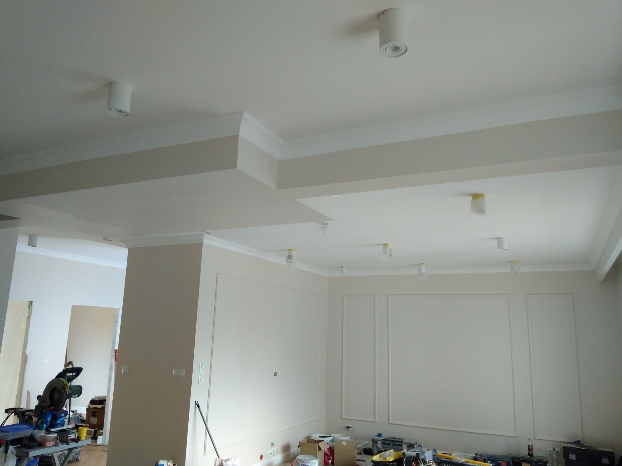 Jasne wnętrze po szpachlowaniu i malowaniu, z dekoracyjnymi listwami ściennymi i sufitowymi, oraz widocznymi narzędziami malarskimi.