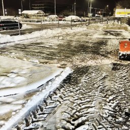 FHU ALEKSANDRA URBAN - Odśnieżony parking nocą, widoczne ślady opon na mokrej nawierzchni, resztki śniegu przy krawężnikach i zaparkowane samochody w tle pod latarniami.