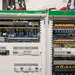 VOLTREND - Rozdzielnica elektryczna Schneider PrismaSeT z widocznymi zabezpieczeniami, kontrolą napięcia, rozłącznikiem głównym oraz okablowaniem w kolorach: żółtym, niebieskim, czarnym i brązowym. Na górze...