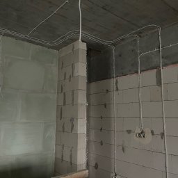 VOLTREND - Surowy stan: białe przewody elektryczne zamocowane do sufitu i ścian z betonu komórkowego w nowym budynku, widoczne puszki instalacyjne.