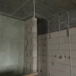 Surowy stan: białe przewody elektryczne zamocowane do sufitu i ścian z betonu komórkowego w nowym budynku, widoczne puszki instalacyjne.