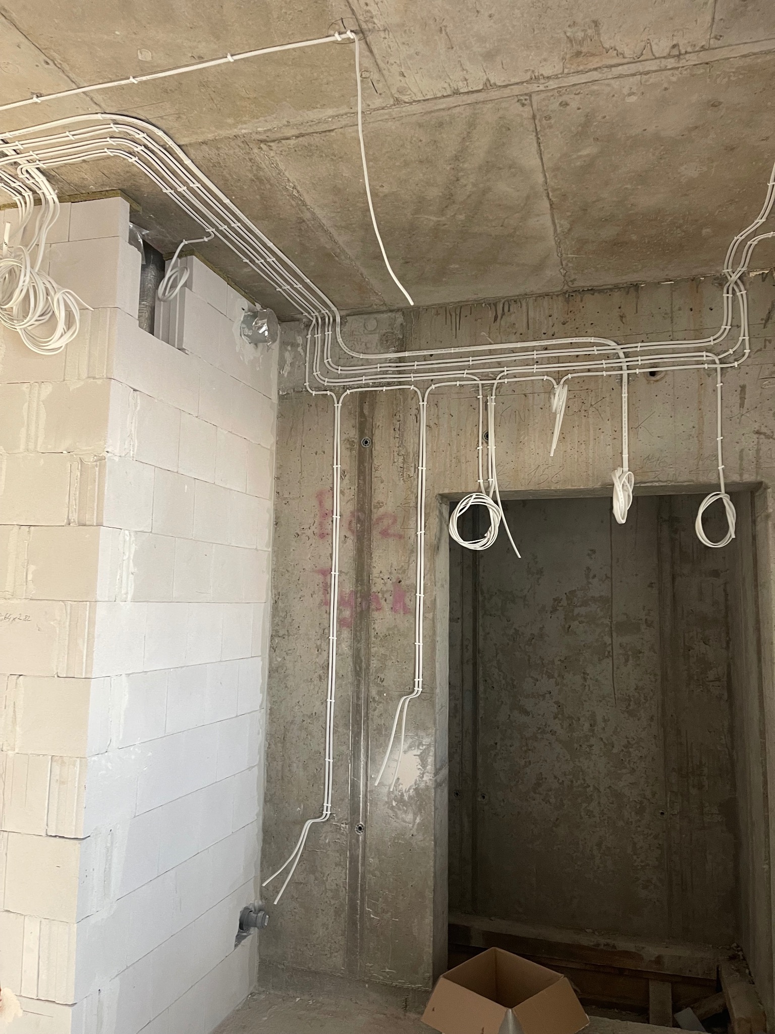 Surowy stan: białe przewody elektryczne ułożone na suficie i ścianach w nowym budynku z betonu komórkowego, widoczne pętle przewodów zwisające z sufitu.