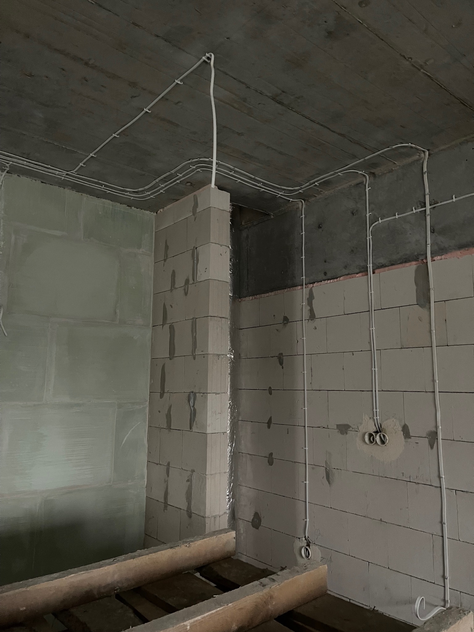 Surowy stan: białe przewody elektryczne zamocowane do sufitu i ścian z betonu komórkowego w nowym budynku, widoczne puszki instalacyjne.