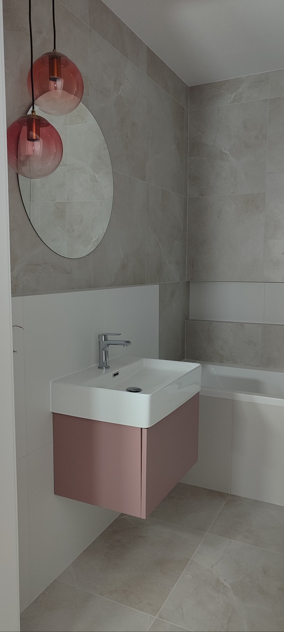 Nowoczesna łazienka z umywalką na szafce w odcieniu pudrowego różu, okrągłe lustro i grafitowe płytki. Minimalistyczny design i subtelne oświetlenie.