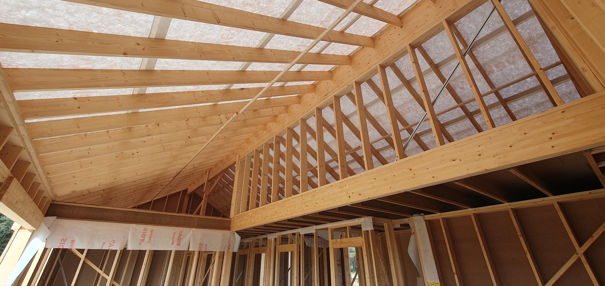 Wnętrze w trakcie budowy: drewniana konstrukcja szkieletowa dachu i ścian z widoczną membraną izolacyjną, jasne drewno, surowe wykończenie.