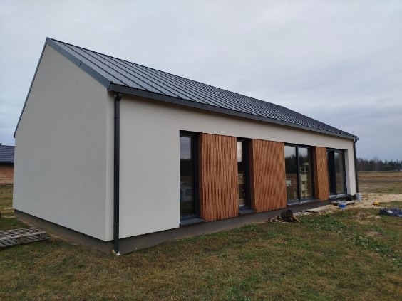 Nowoczesny dom z jasną elewacją i drewnianymi panelami okiennymi, widok z zewnątrz w pochmurny dzień. Minimalistyczny design z ciemnym dachem.