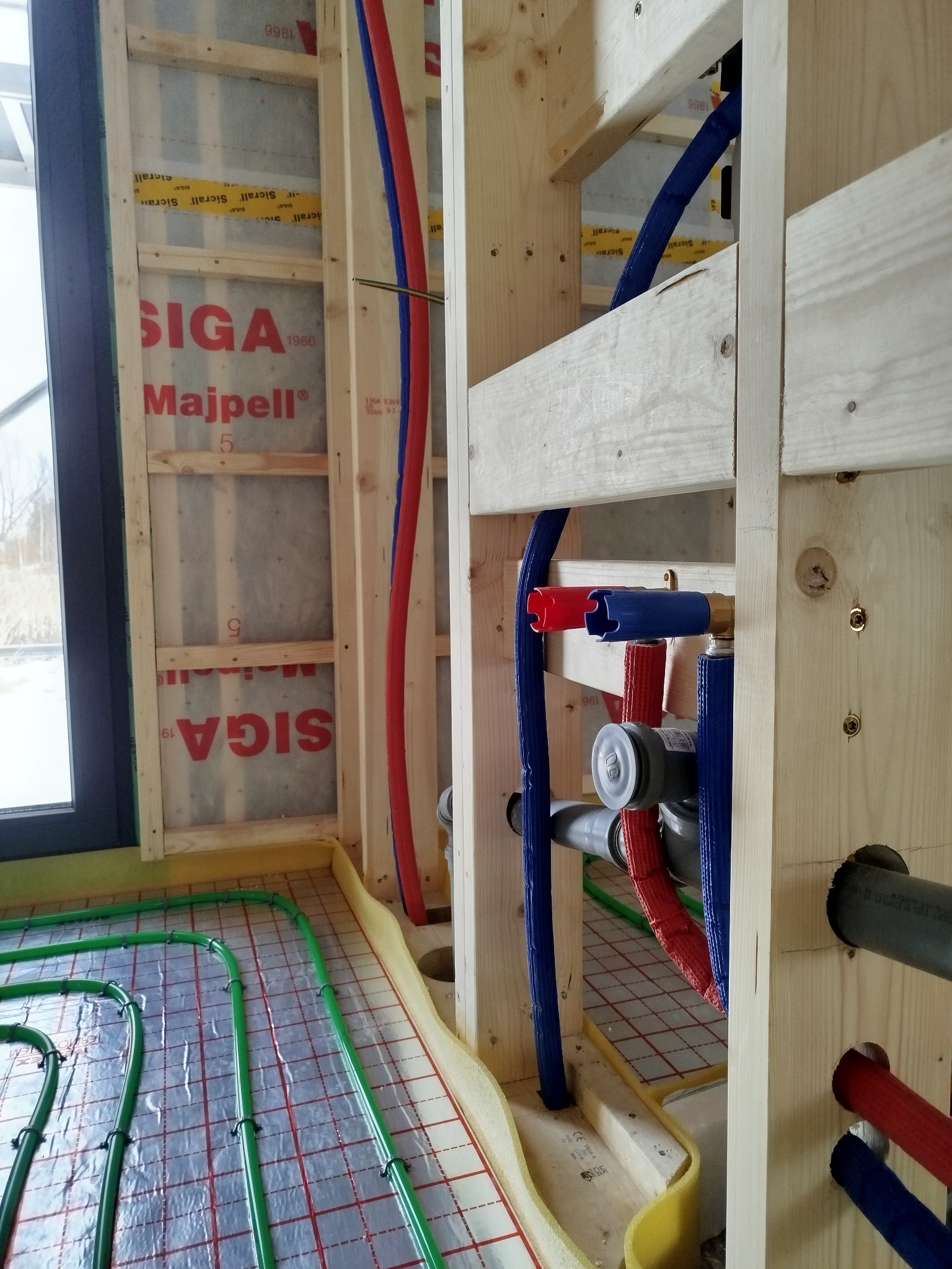 Instalacja ogrzewania podłogowego i rur wodnych w drewnianej konstrukcji domu. Widoczne elementy izolacji i mocowania rur. Detal budowy.