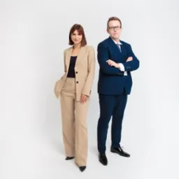 Profesjonalny portret zespołowy: kobieta w beżowym garniturze i mężczyzna w granatowym garniturze, oboje stoją na białym tle, uśmiechają się i patrzą w kamerę.