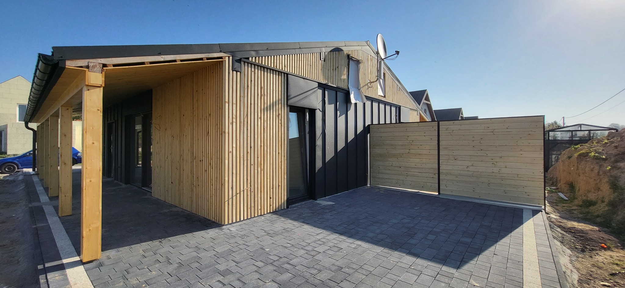 Nowoczesny dom z drewnianą elewacją, czarnymi akcentami i brukowanym podjazdem, widok z zewnątrz w słoneczny dzień.