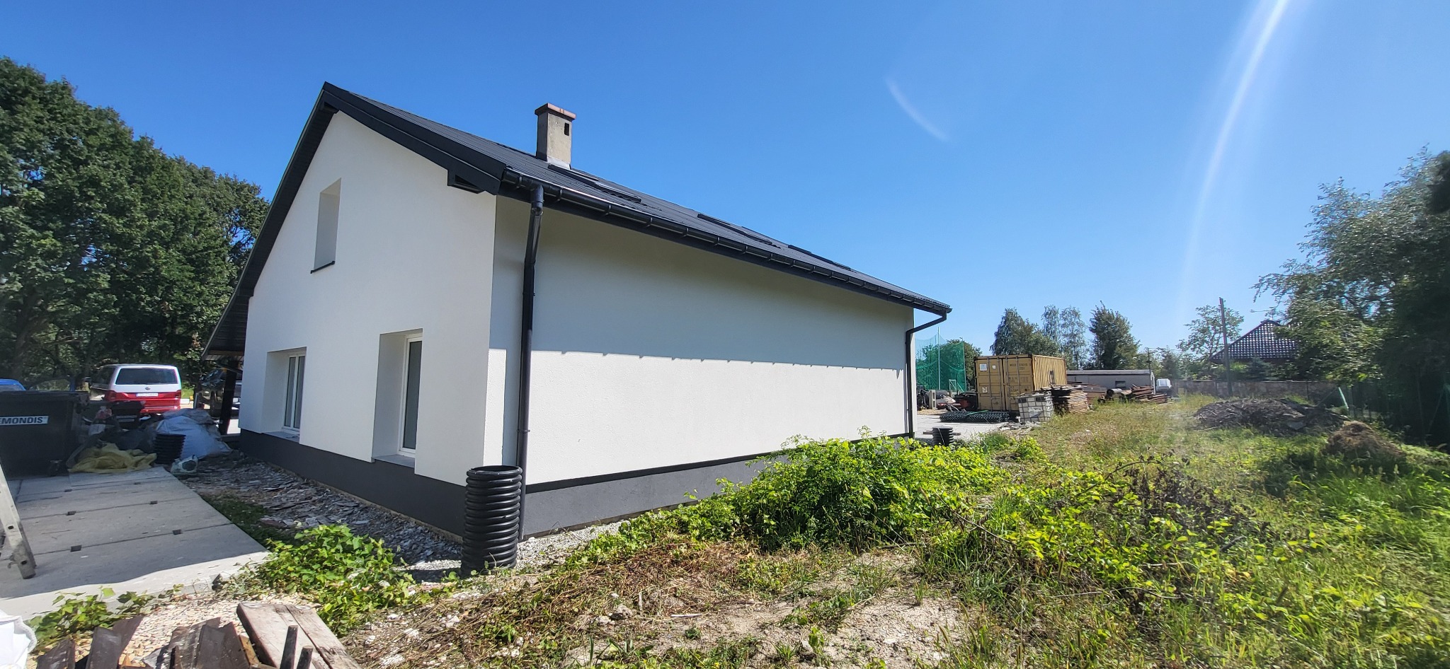 Ocieplony i pomalowany na biało dom jednorodzinny w Żorach, widok z boku na elewację i fragment dachu, z widocznym fragmentem ogrodu i kontenerem w tle.