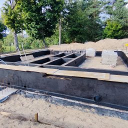 MTM-BUDOWA SPÓŁKA Z OGRANICZONĄ ODPOWIEDZIALNOŚCIĄ - Fundamenty domu jednorodzinnego po izolacji przeciwwilgociowej, widoczne zbrojenia i przygotowane otwory wentylacyjne. Prace ziemne w toku.