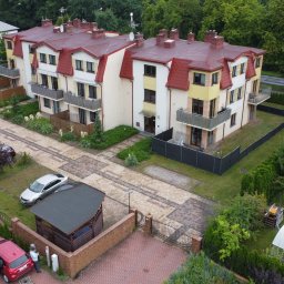 MTM-BUDOWA SPÓŁKA Z OGRANICZONĄ ODPOWIEDZIALNOŚCIĄ - Wielorodzinny budynek z czerwonym dachem, widok z góry. Uwagę zwraca starannie zagospodarowany teren z parkingiem i zielenią. Widoczny fragment osiedla.